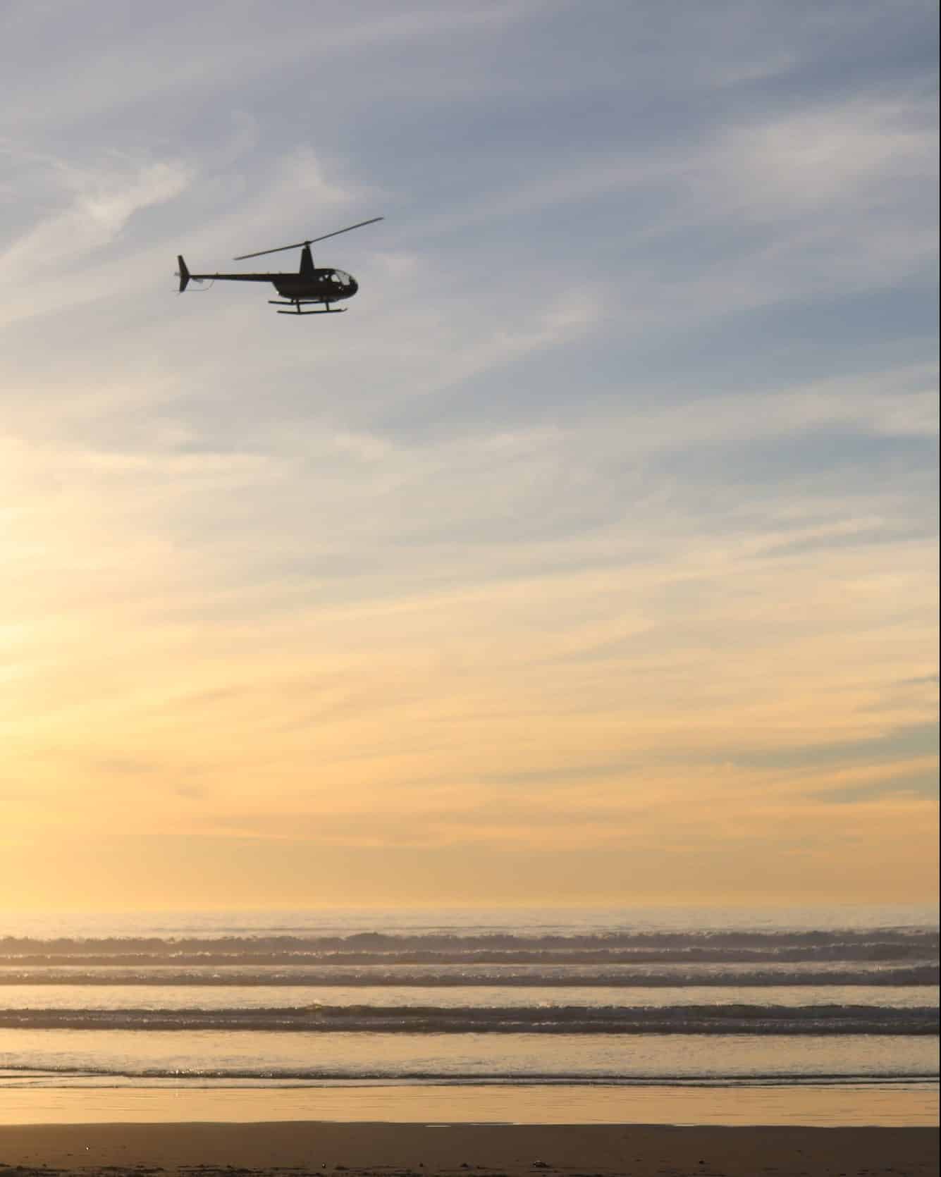 Silhouette of a helicopter flying over the Baja California beach during the orange sunset