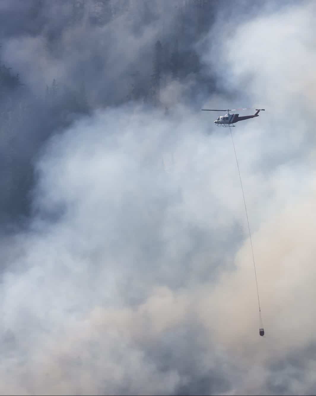 Wildfire Service Helicopter flying over BC Forest Fire and Smoke on the mountain near Hope